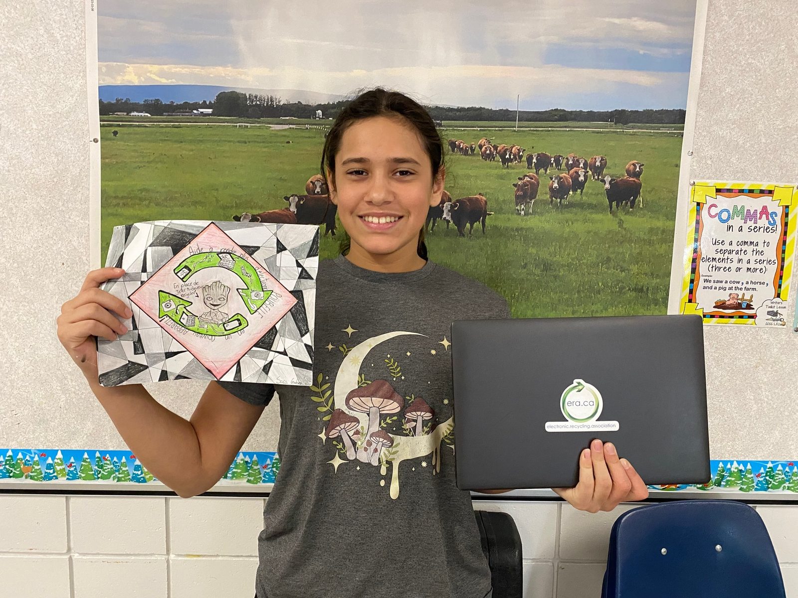 A student holding a refurbished ERA laptop and a drawing about technology reuse